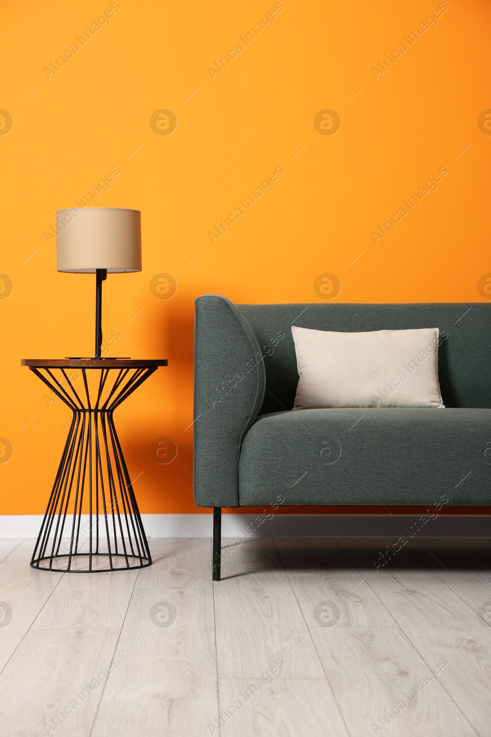 Photo of Stylish sofa with cushion and lamp on side table near orange wall