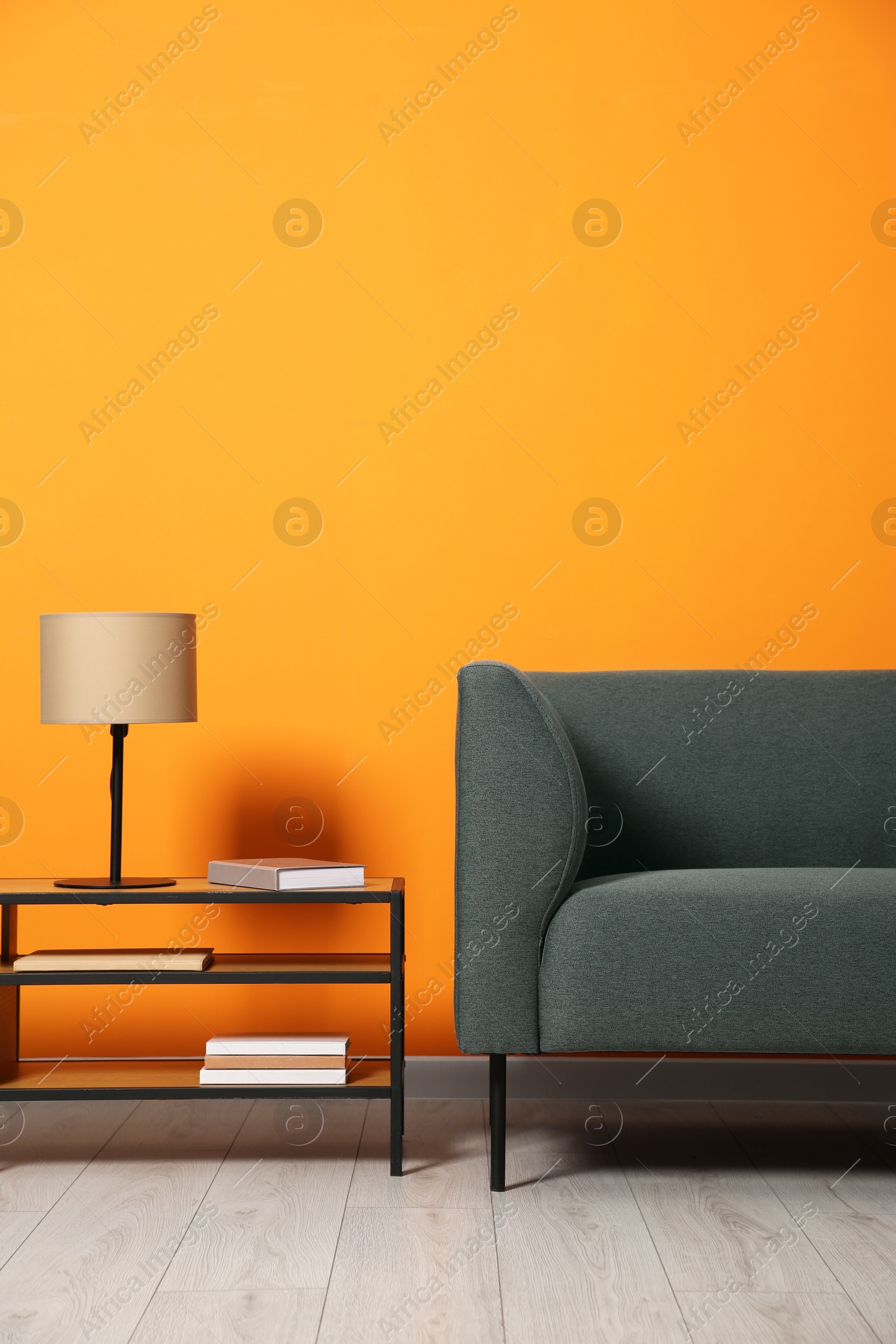 Photo of Stylish sofa and lamp with books on coffee table near orange wall