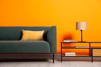 Photo of Stylish sofa with cushion and lamp on coffee table near orange wall