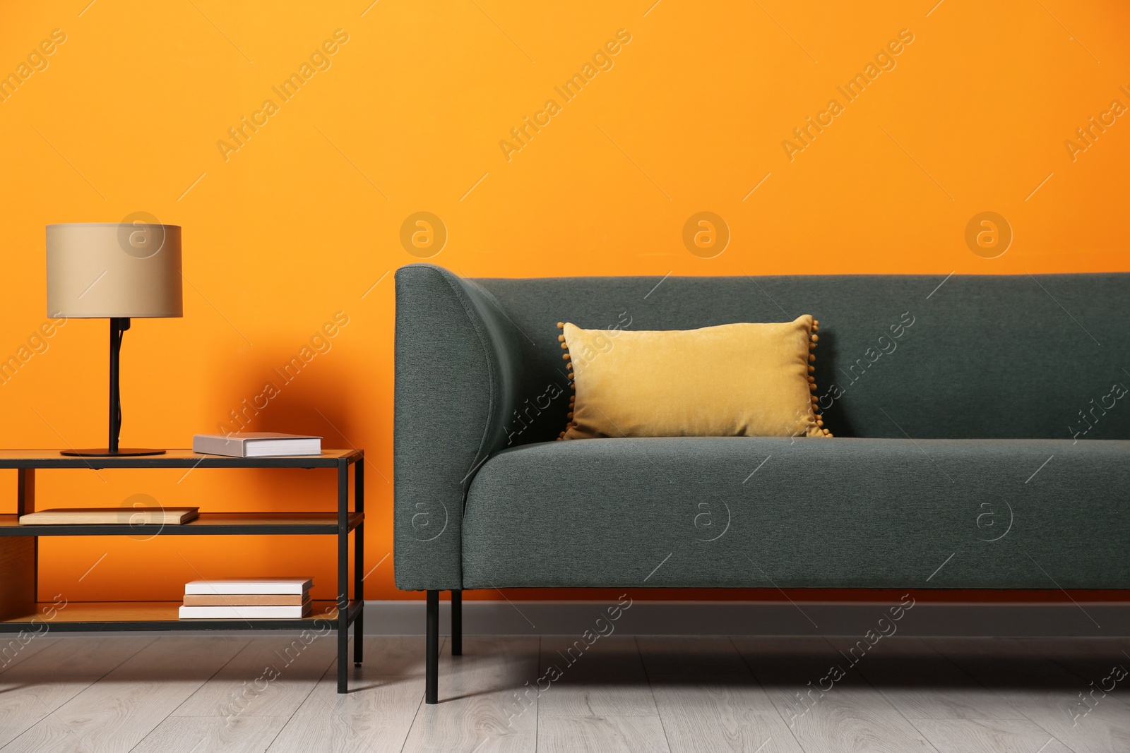 Photo of Stylish sofa with cushion and lamp on coffee table near orange wall