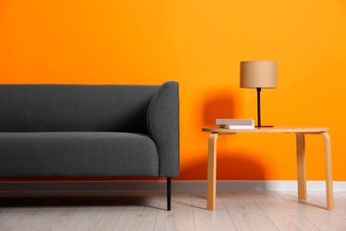 Photo of Stylish sofa, lamp and books on coffee table near orange wall