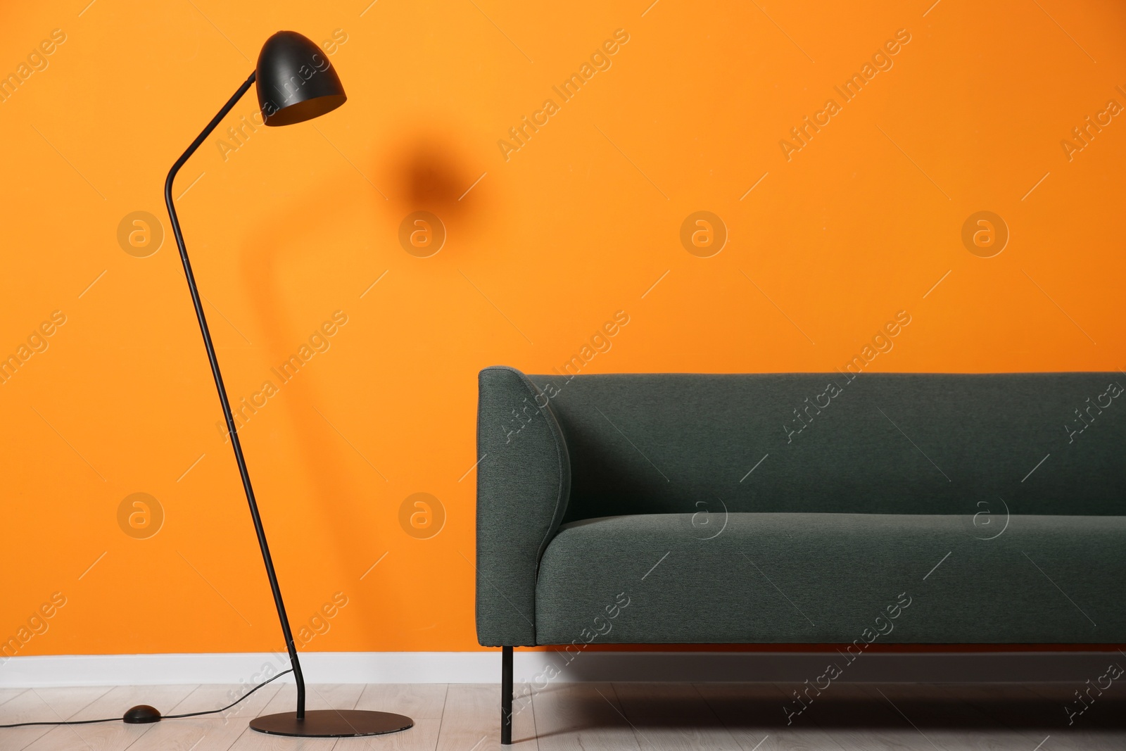 Photo of Stylish sofa and floor lamp near orange wall