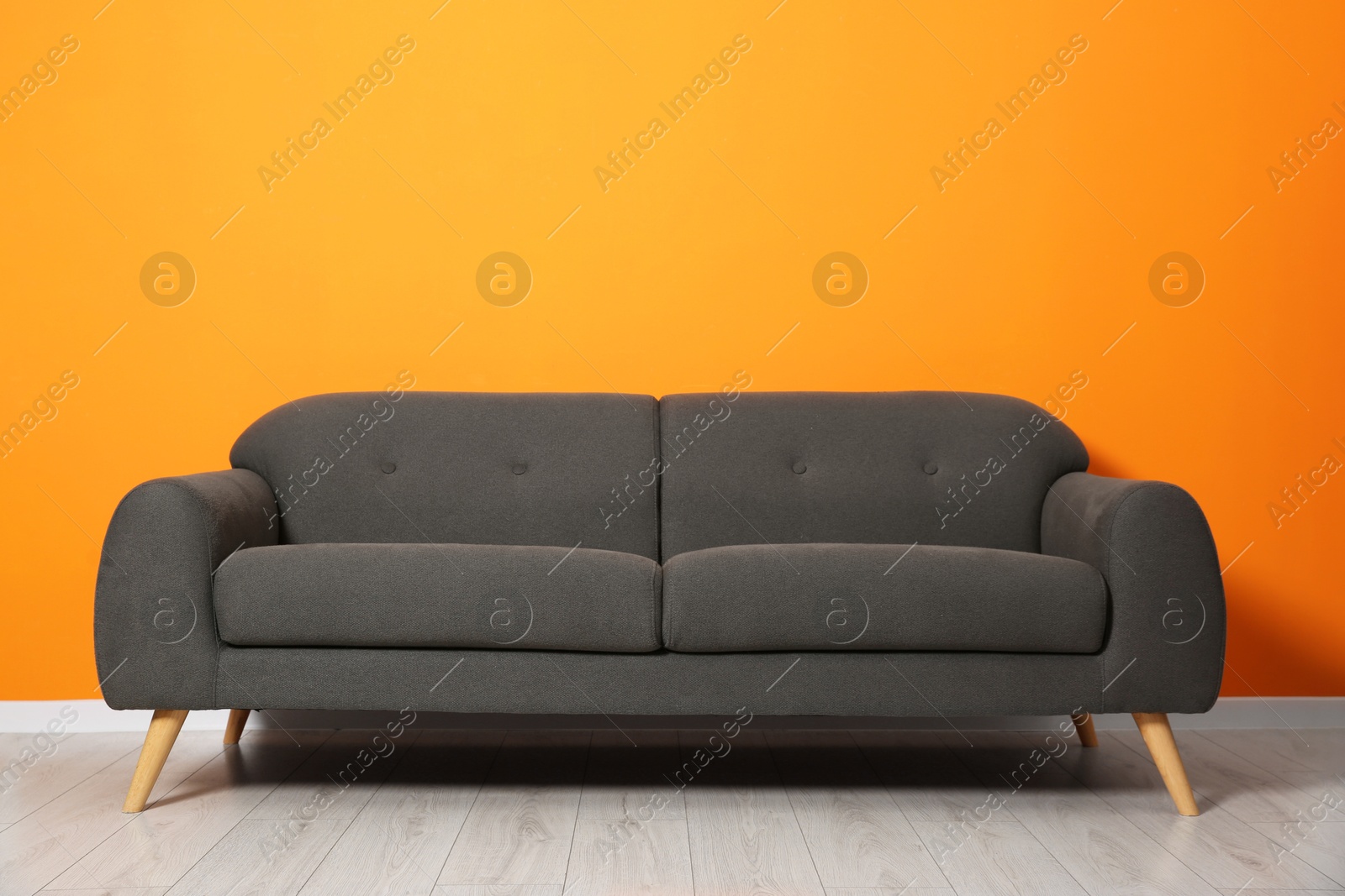 Photo of One stylish grey sofa near orange wall