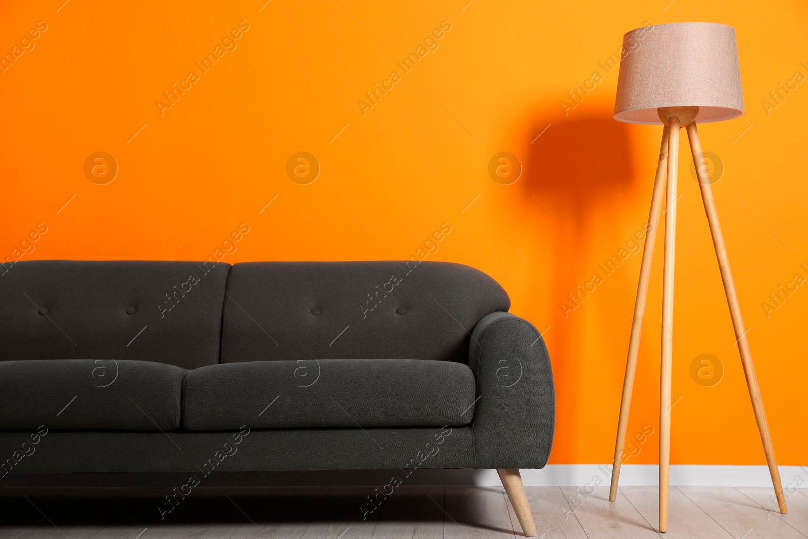 Photo of Stylish sofa and floor lamp near orange wall