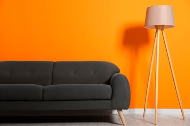 Photo of Stylish sofa and floor lamp near orange wall