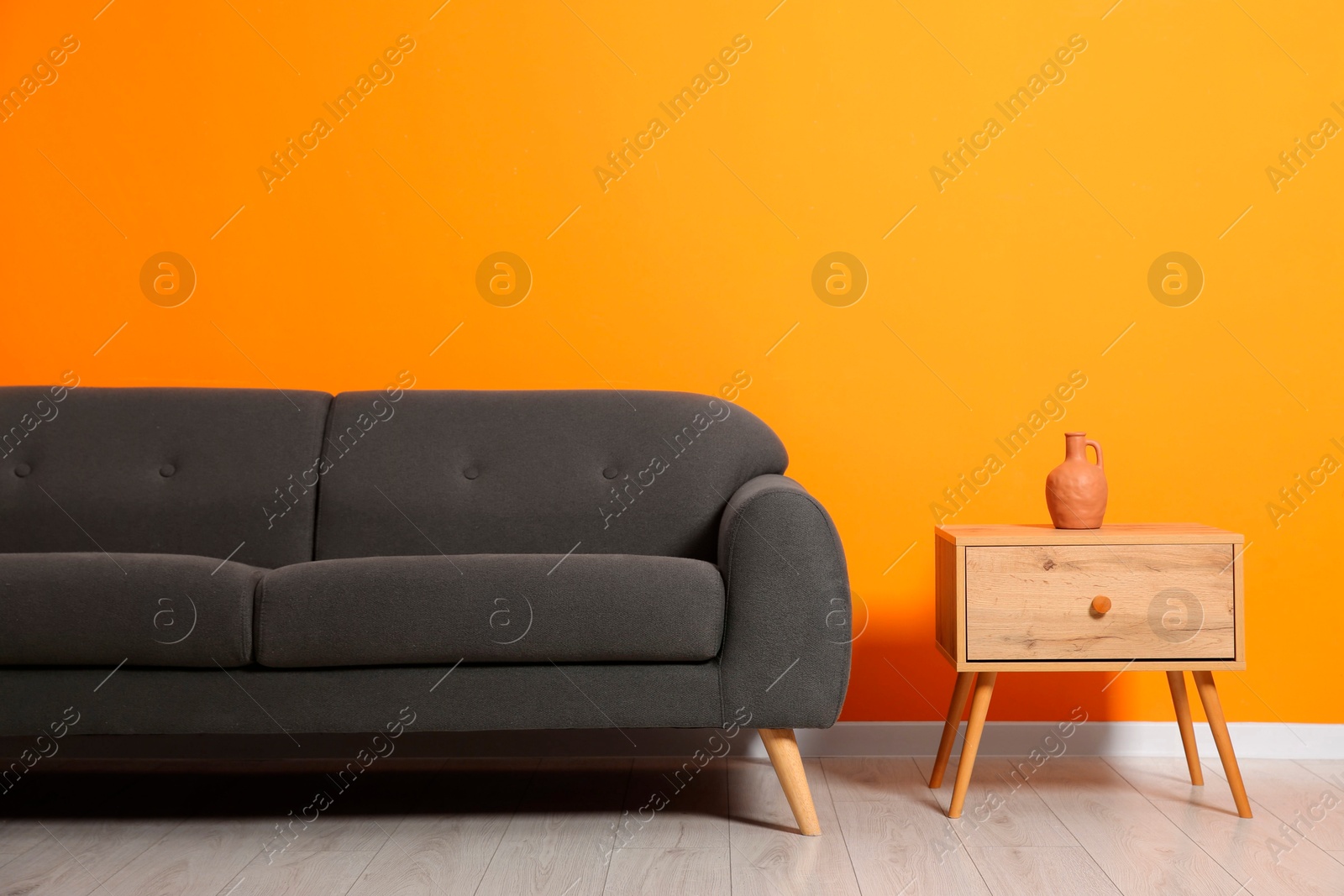 Photo of Stylish grey sofa and decor element on side table near orange wall