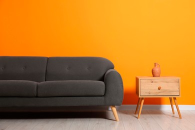 Photo of Stylish grey sofa and decor element on side table near orange wall