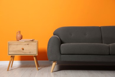 Photo of Stylish sofa and books on side table near orange wall