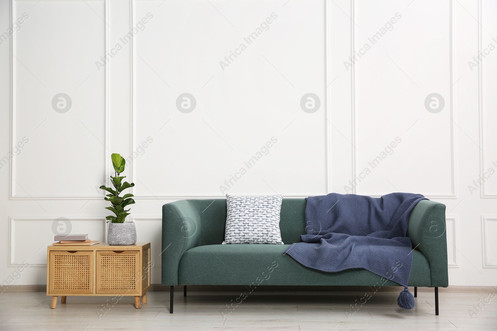 Photo of Stylish sofa with cushion, plant and books on side table near white wall