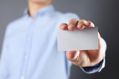 Man holding blank business card on grey background, closeup. Mockup for design