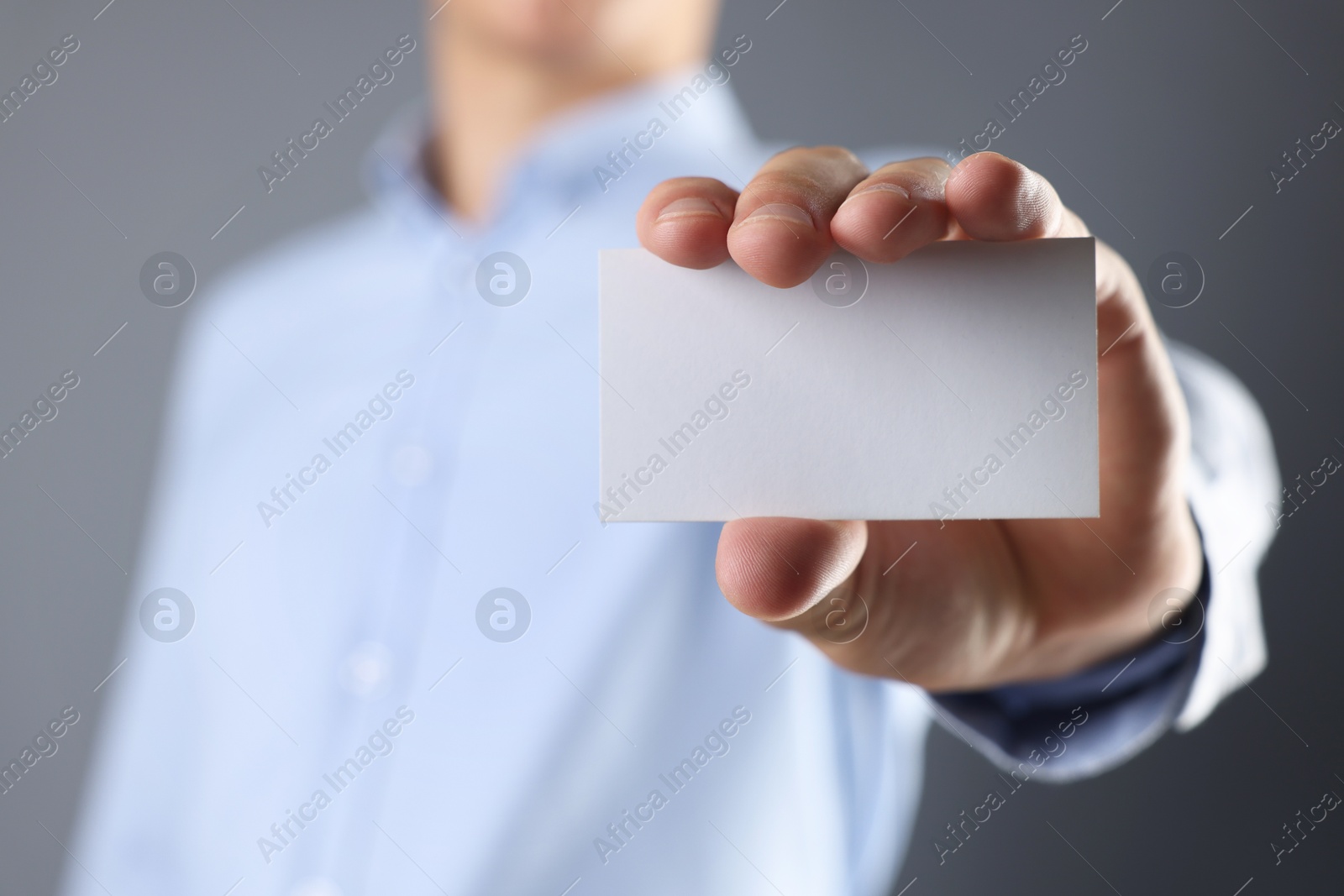 Photo of Man holding blank business card on grey background, closeup. Mockup for design