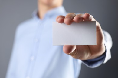 Man holding blank business card on grey background, closeup. Mockup for design