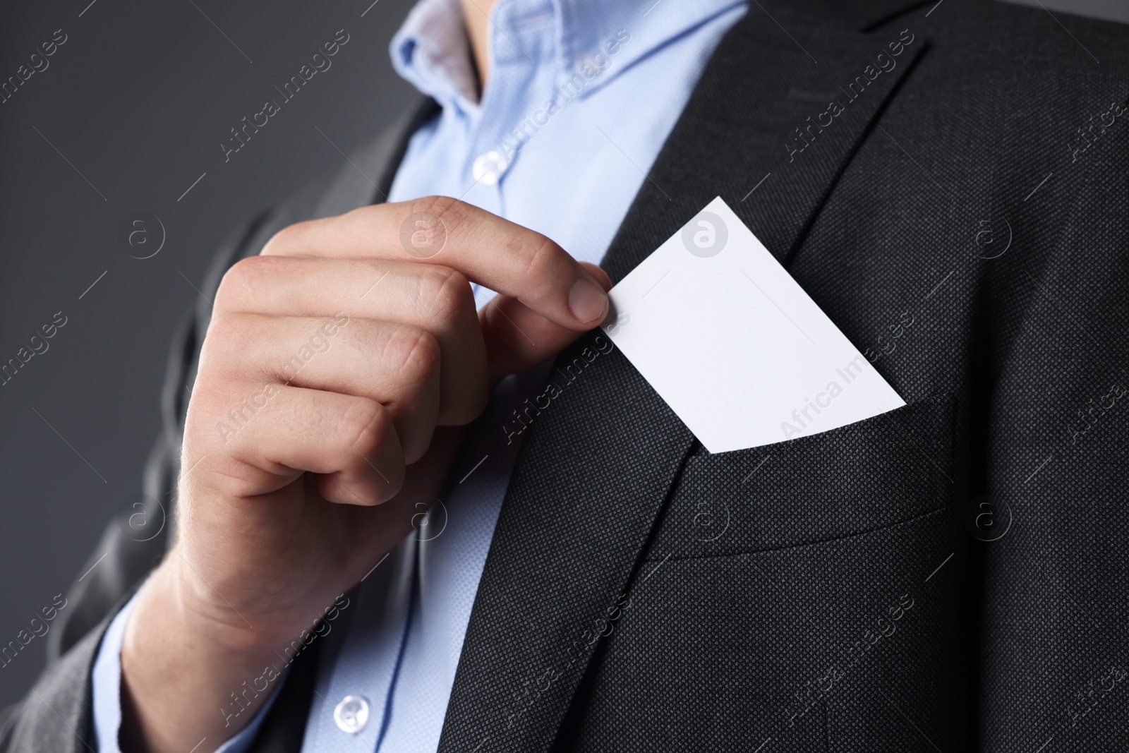 Photo of Man taking blank business card from pocket of his jacket on grey background, closeup. Mockup for design