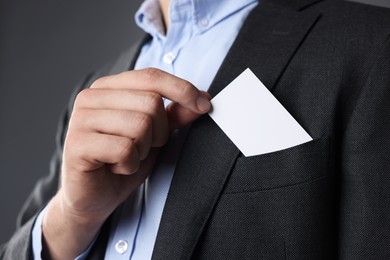 Photo of Man taking blank business card from pocket of his jacket on grey background, closeup. Mockup for design