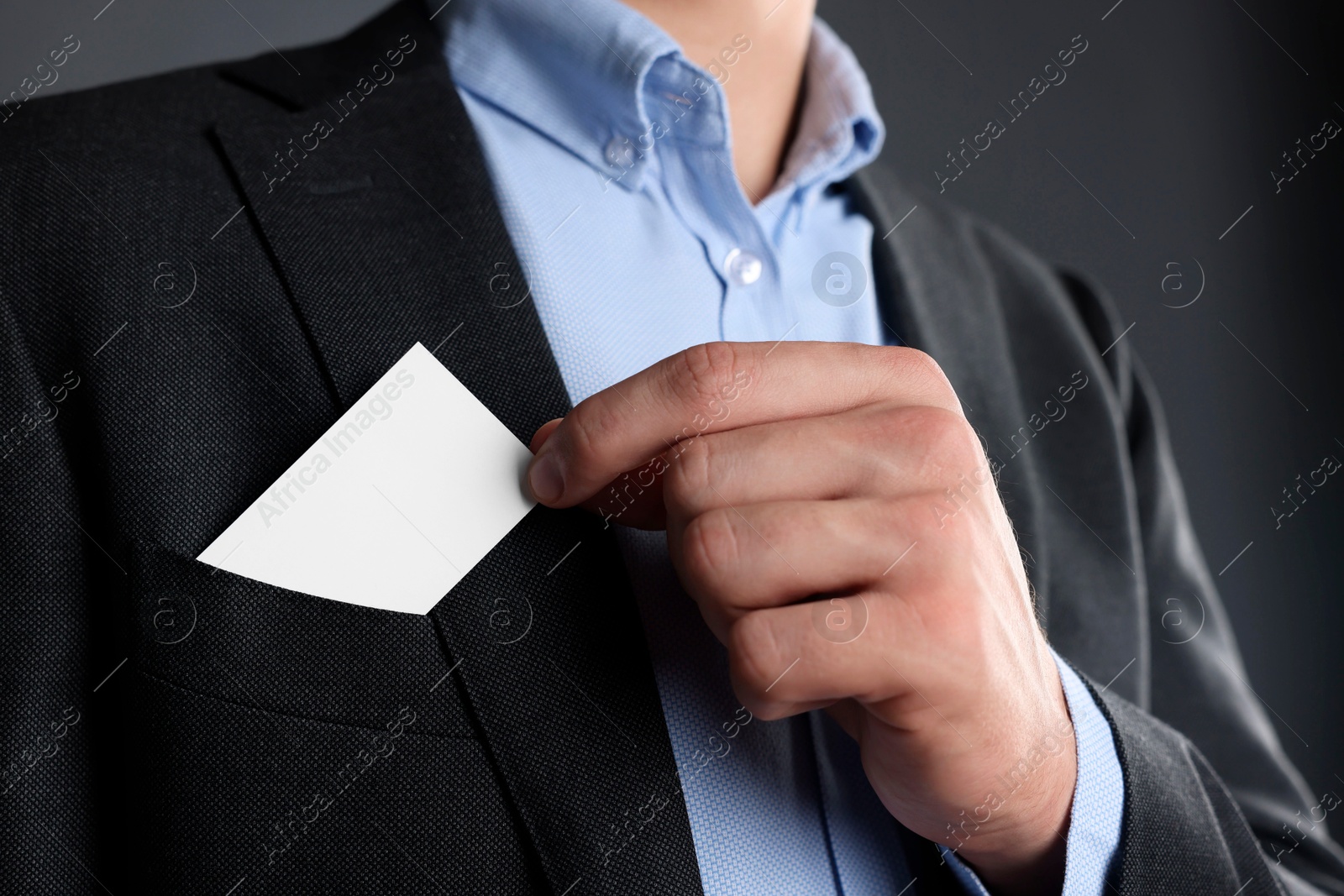 Photo of Man taking blank business card from pocket of his jacket on grey background, closeup. Mockup for design