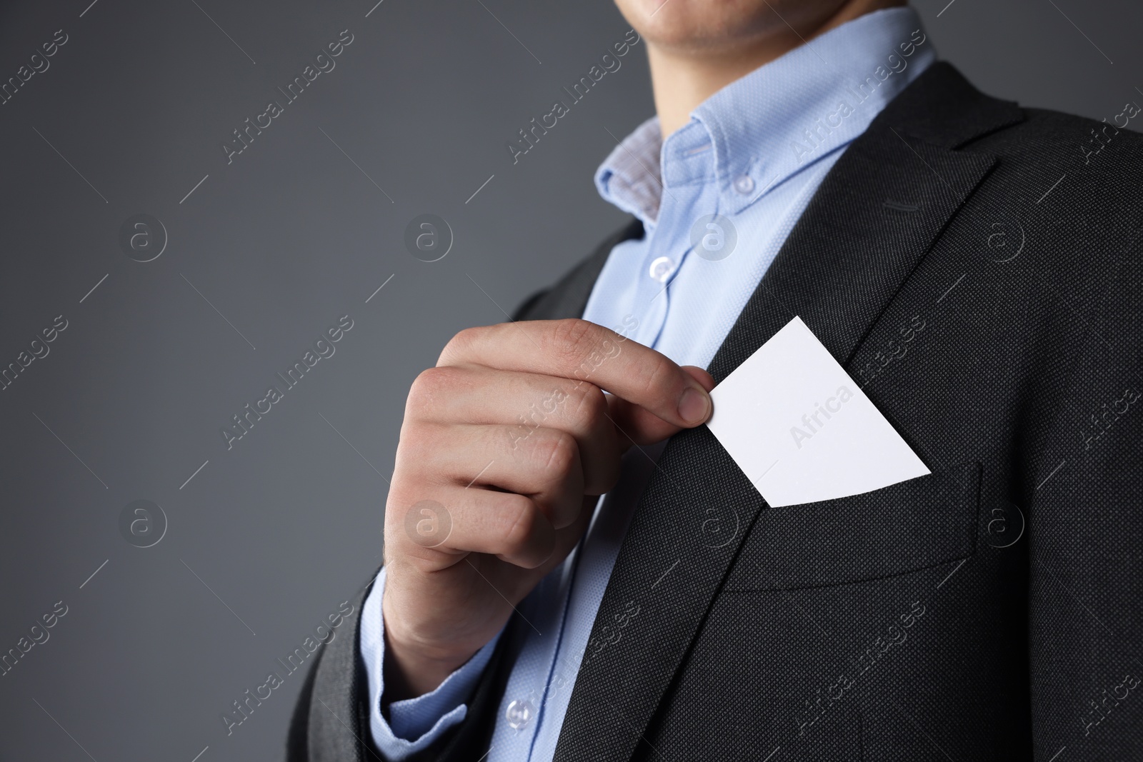 Photo of Man taking blank business card from pocket of his jacket on grey background, closeup. Mockup for design