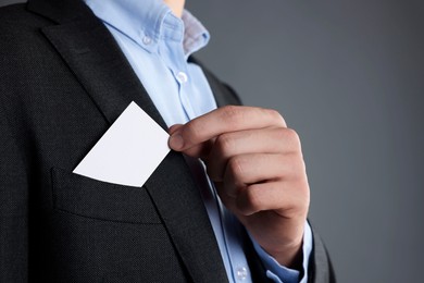 Man taking blank business card from pocket of his jacket on grey background, closeup. Mockup for design