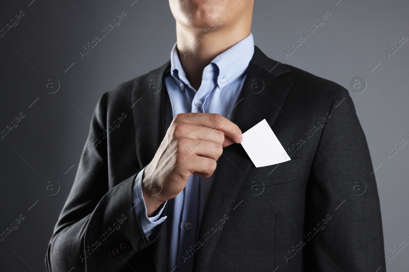 Photo of Man taking blank business card from pocket of his jacket on grey background, closeup. Mockup for design