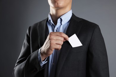 Man taking blank business card from pocket of his jacket on grey background, closeup. Mockup for design