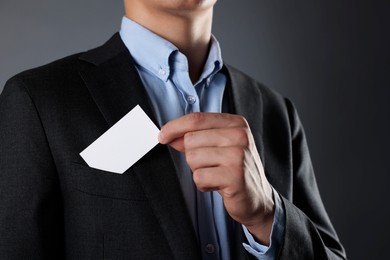 Photo of Man taking blank business card from pocket of his jacket on grey background, closeup. Mockup for design