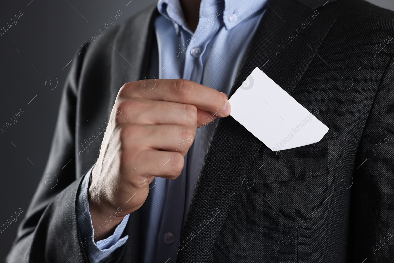 Photo of Man taking blank business card from pocket of his jacket on grey background, closeup. Mockup for design