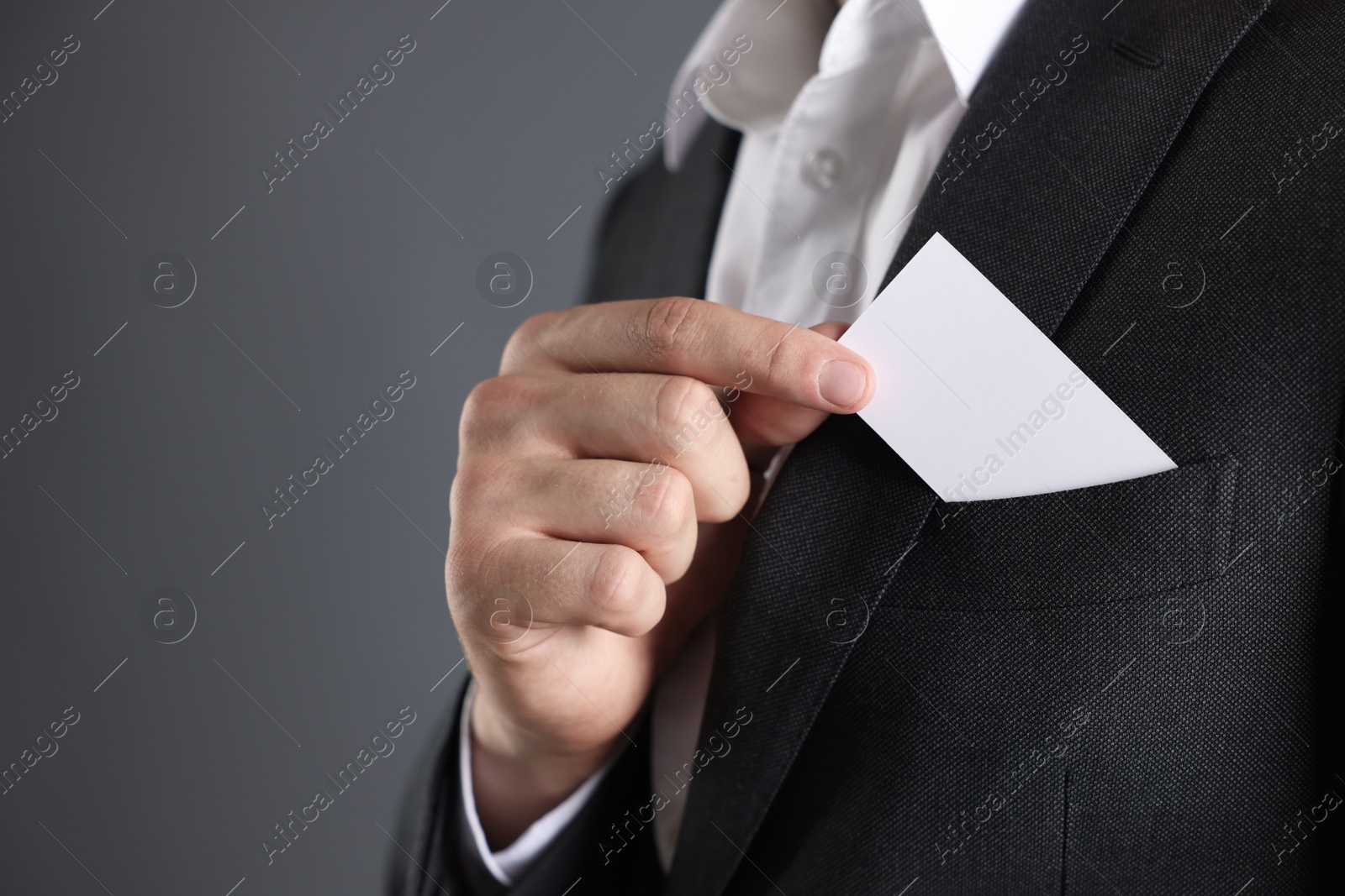 Photo of Man taking blank business card from pocket of his jacket on grey background, closeup. Mockup for design