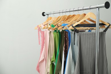 Photo of Many chef's aprons on clothing rack near light grey wall, space for text