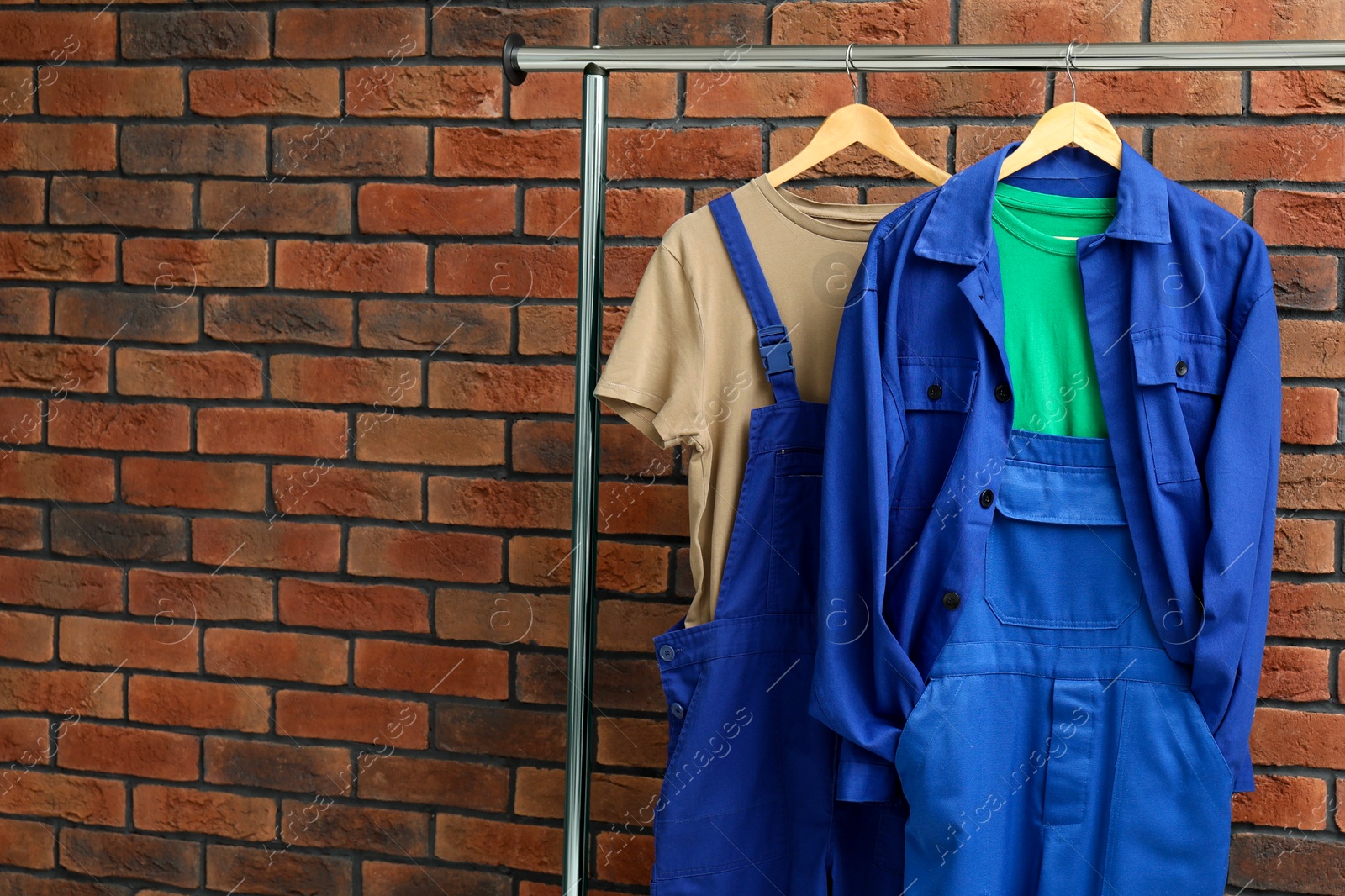 Photo of Workers' uniforms on clothing rack near brick wall, space for text