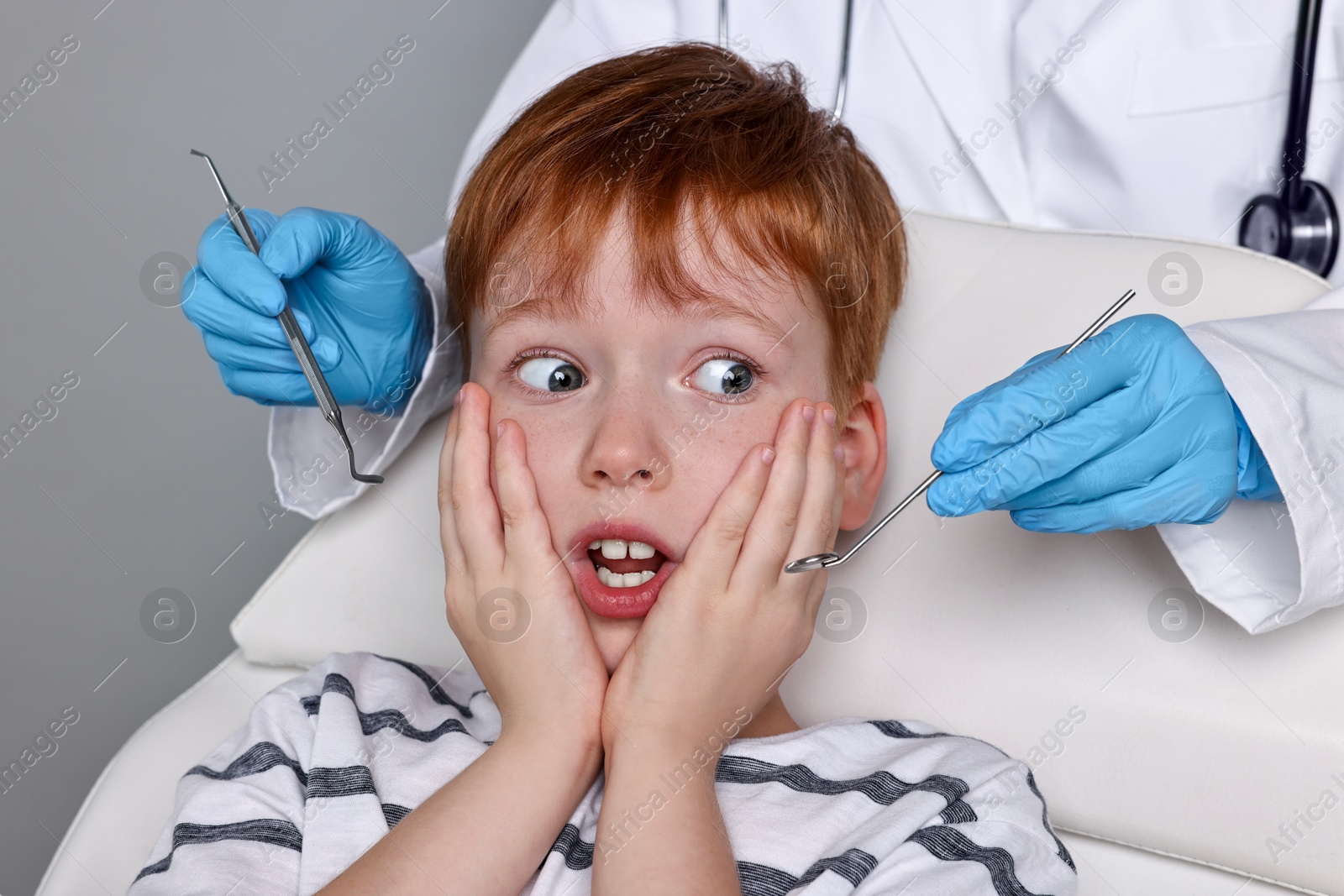 Photo of Dental phobia. Dentist working with scared little boy on grey background