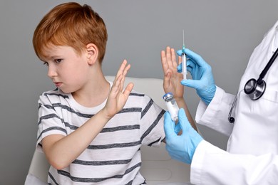 Dental phobia. Scared boy making stop gesture near dentist with syringe and vial on grey background