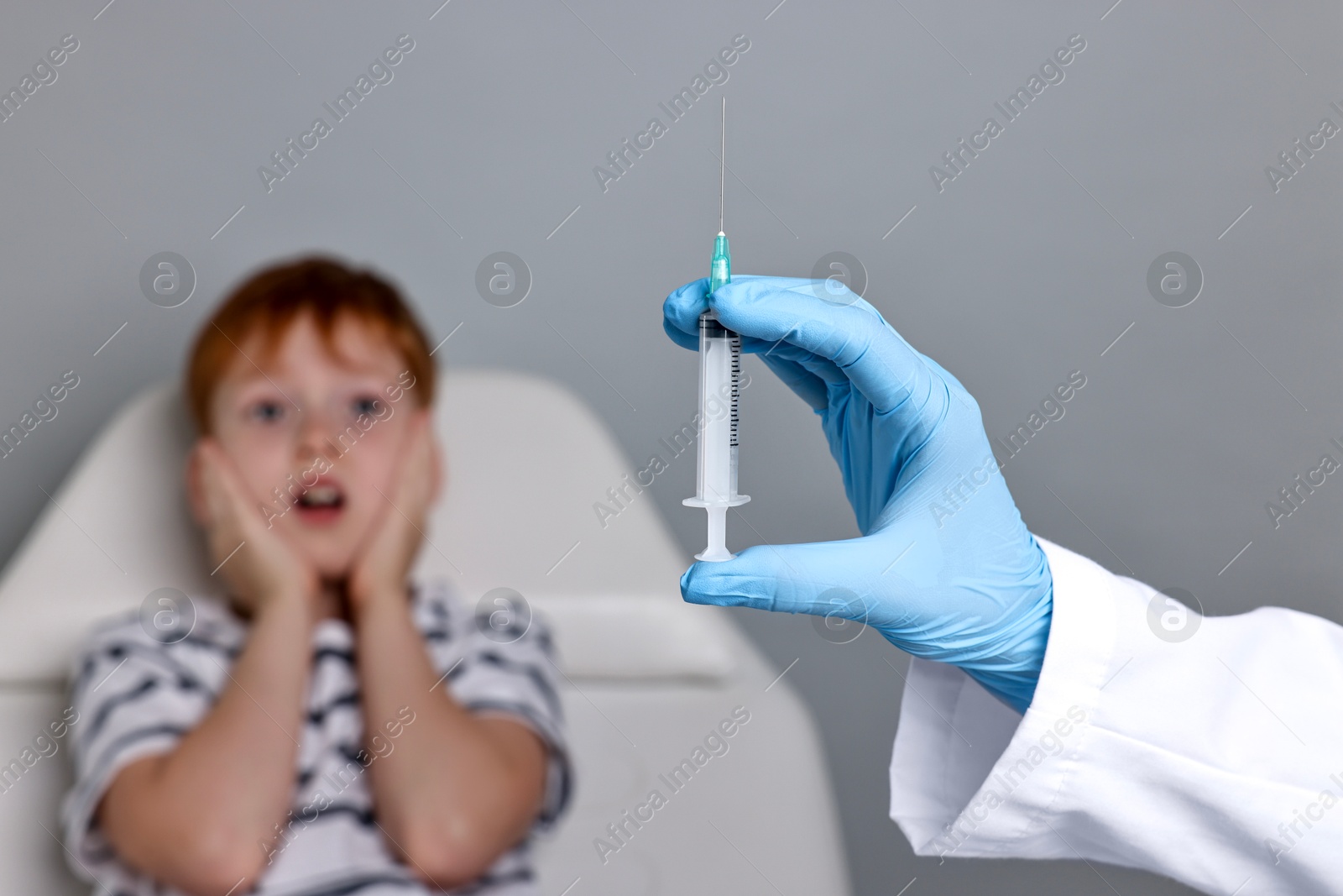 Photo of Dental phobia. Dentist with syringe near scared boy on grey background, selective focus