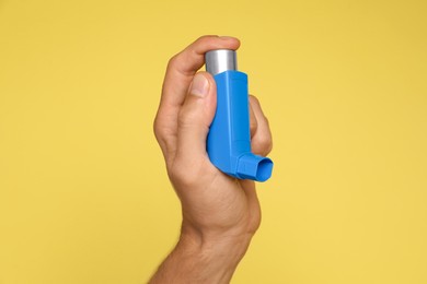 Man holding asthma inhaler on yellow background, closeup