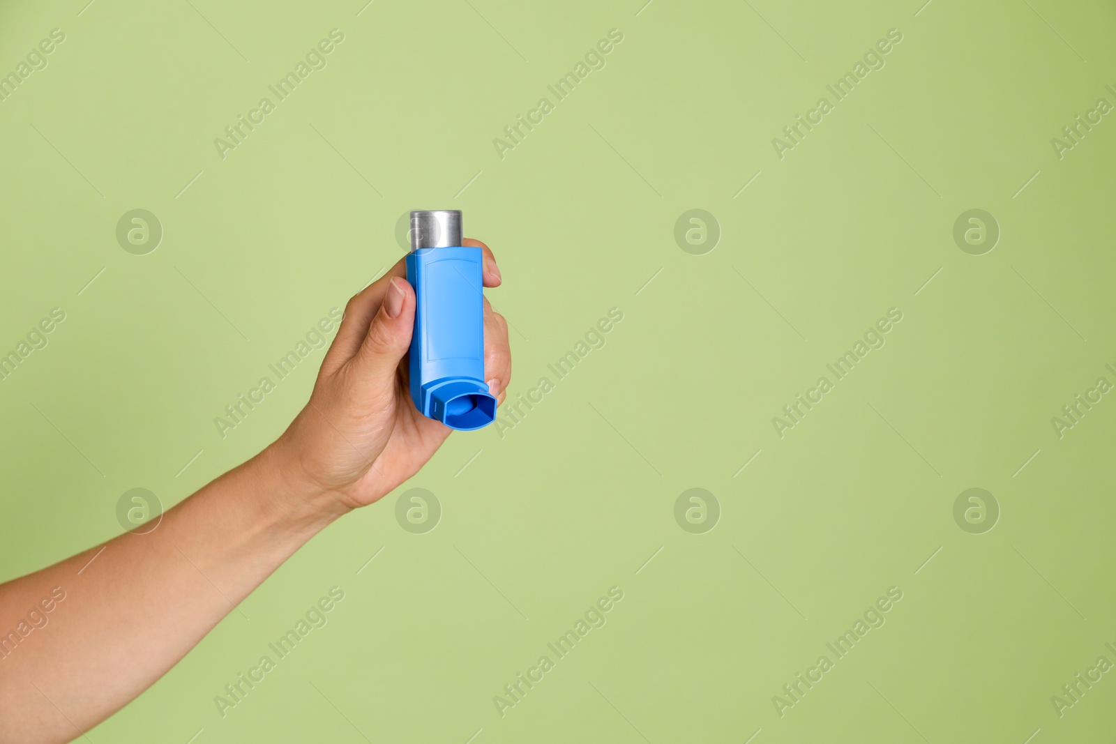 Photo of Woman holding asthma inhaler on olive background, closeup. Space for text