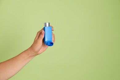 Woman holding asthma inhaler on olive background, closeup. Space for text