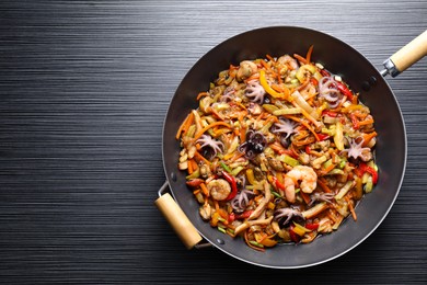 Photo of Stir-fry sea food in wok on black wooden table, top view. Space for text