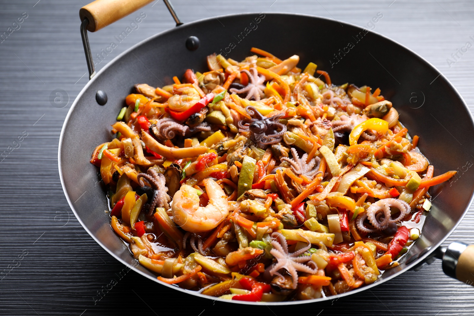 Photo of Stir-fry sea food in wok on black wooden table, closeup