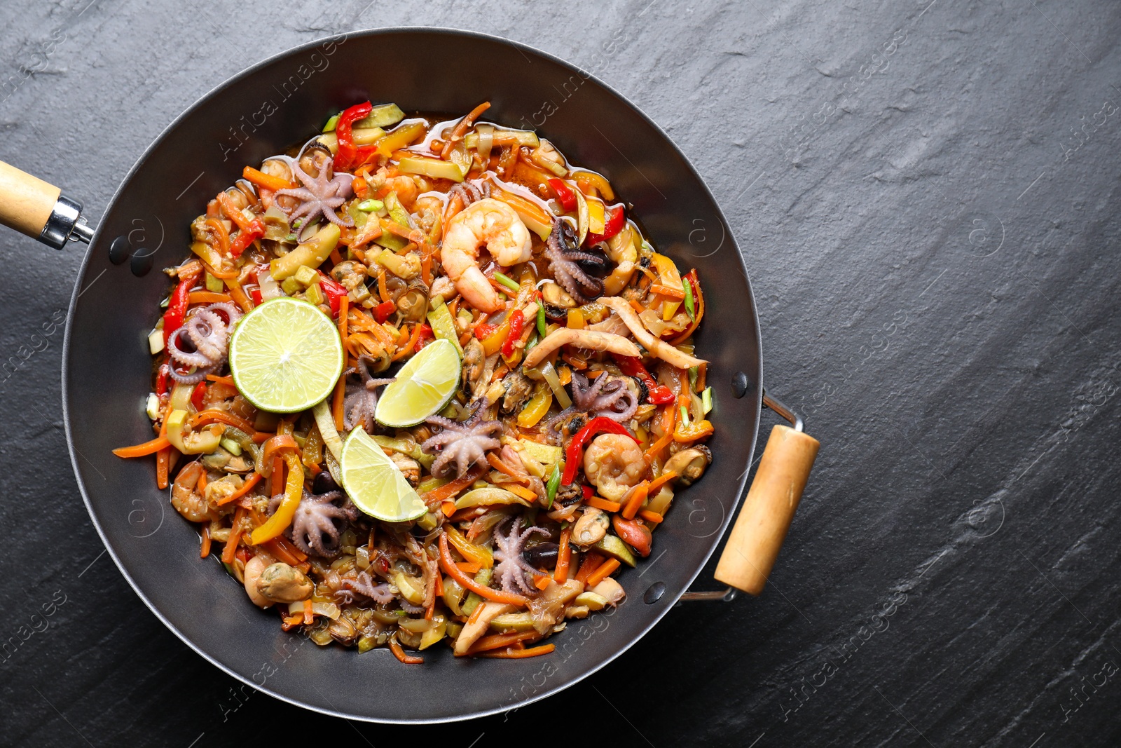 Photo of Stir-fry sea food in wok on grey textured table, top view