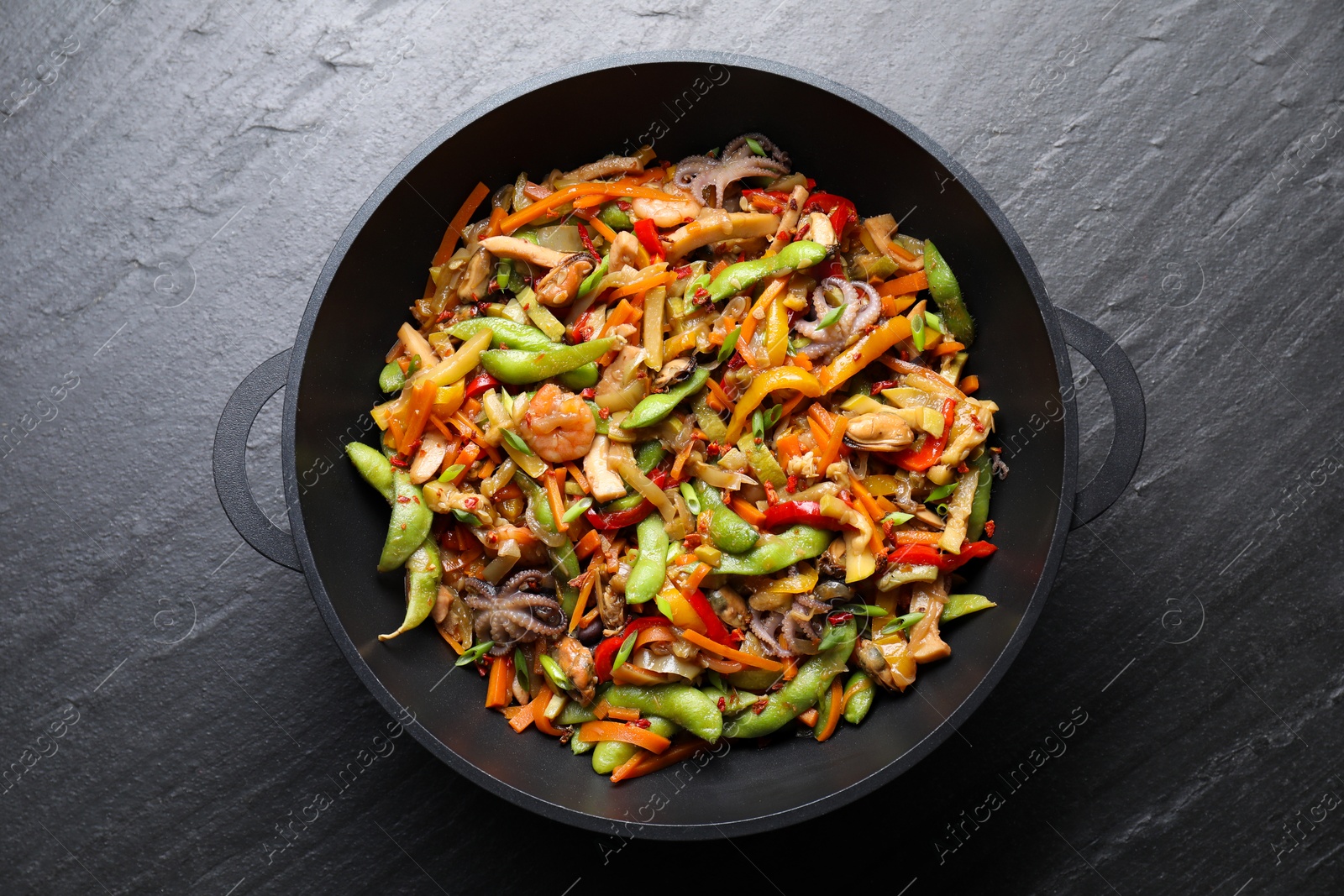 Photo of Stir-fry sea food in wok on grey textured table, top view