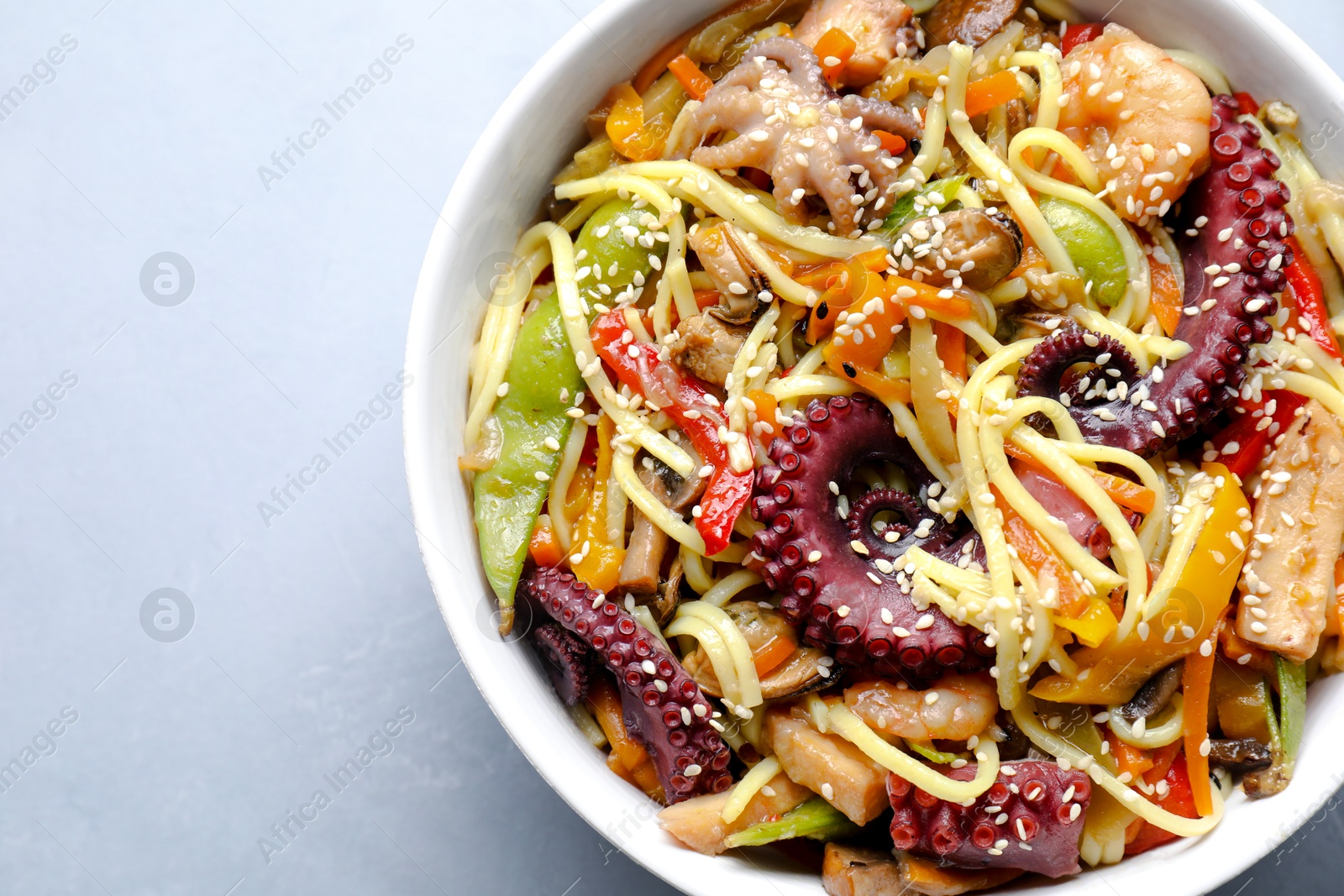 Photo of Stir-fry noodles with sea food in bowl on light grey table, top view. Space for text