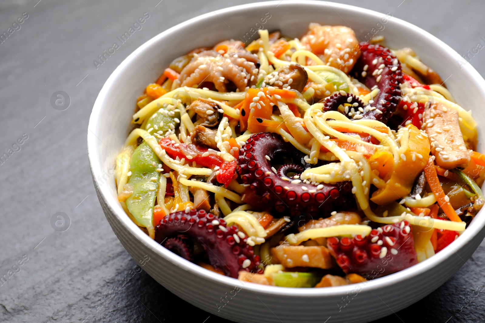 Photo of Stir-fry noodles with sea food in bowl on grey table, closeup