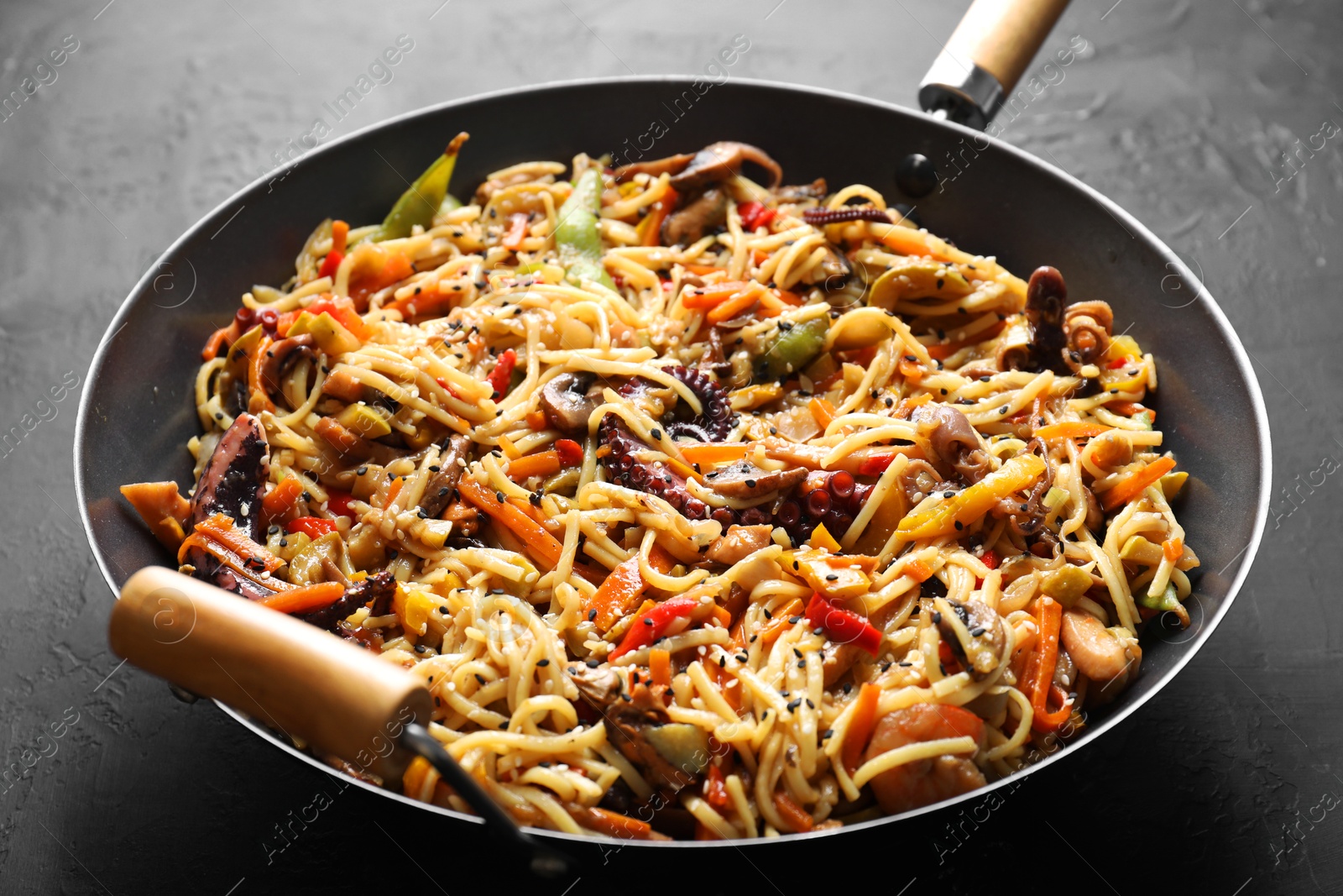 Photo of Stir-fry noodles with sea food and vegetables in wok on dark textured table, closeup