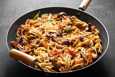 Photo of Stir-fry noodles with sea food and vegetables in wok on dark textured table, closeup