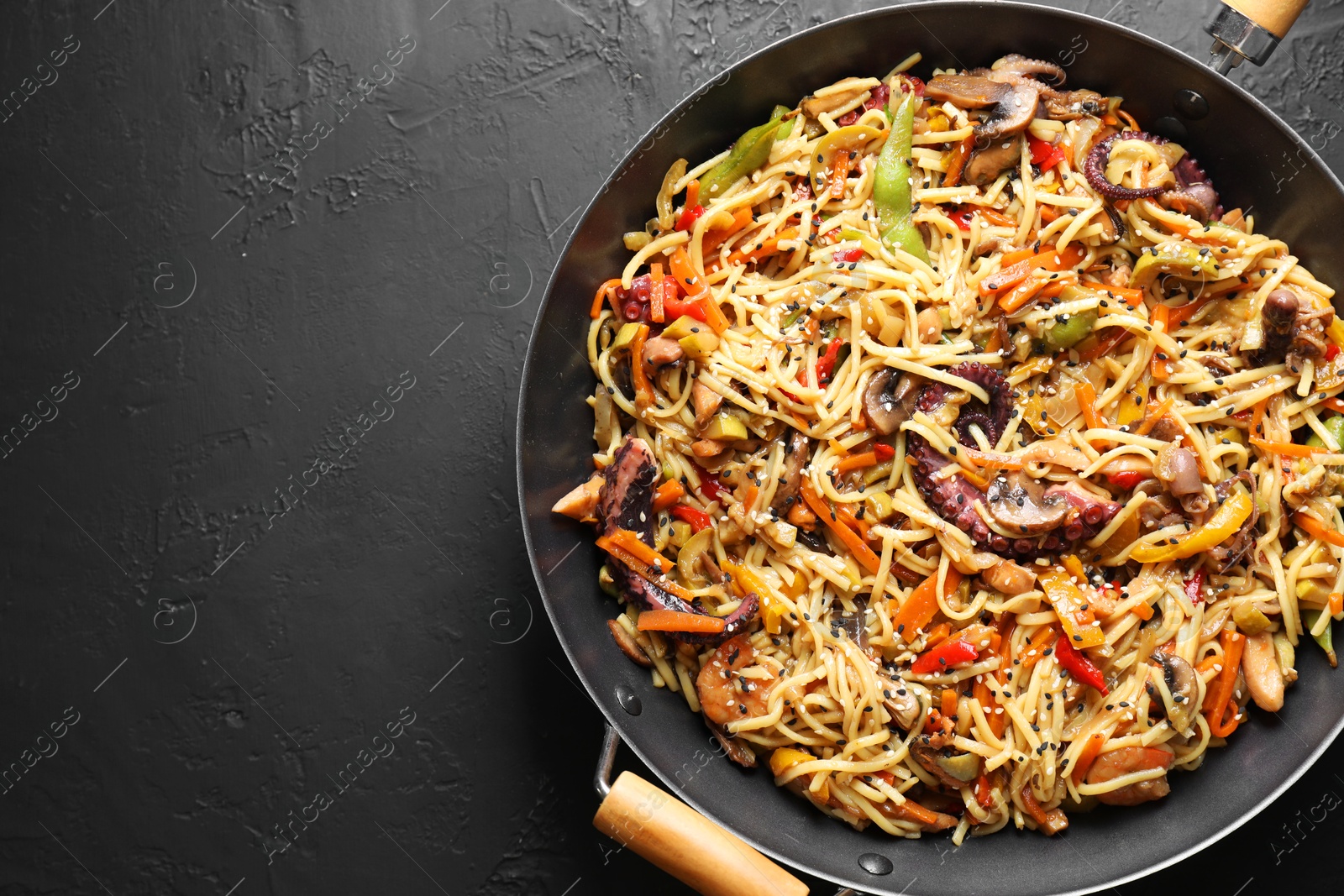 Photo of Stir-fry noodles with sea food and vegetables in wok on dark textured table, top view. Space for text