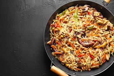 Stir-fry noodles with sea food and vegetables in wok on dark textured table, top view. Space for text