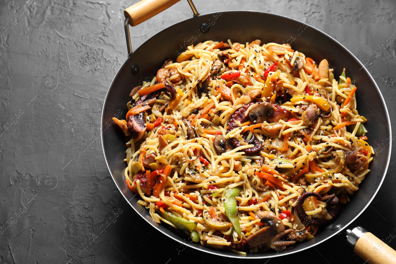 Photo of Stir-fry noodles with sea food and vegetables in wok on dark textured table, closeup