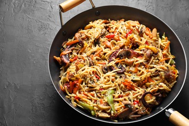 Stir-fry noodles with sea food and vegetables in wok on dark textured table, closeup