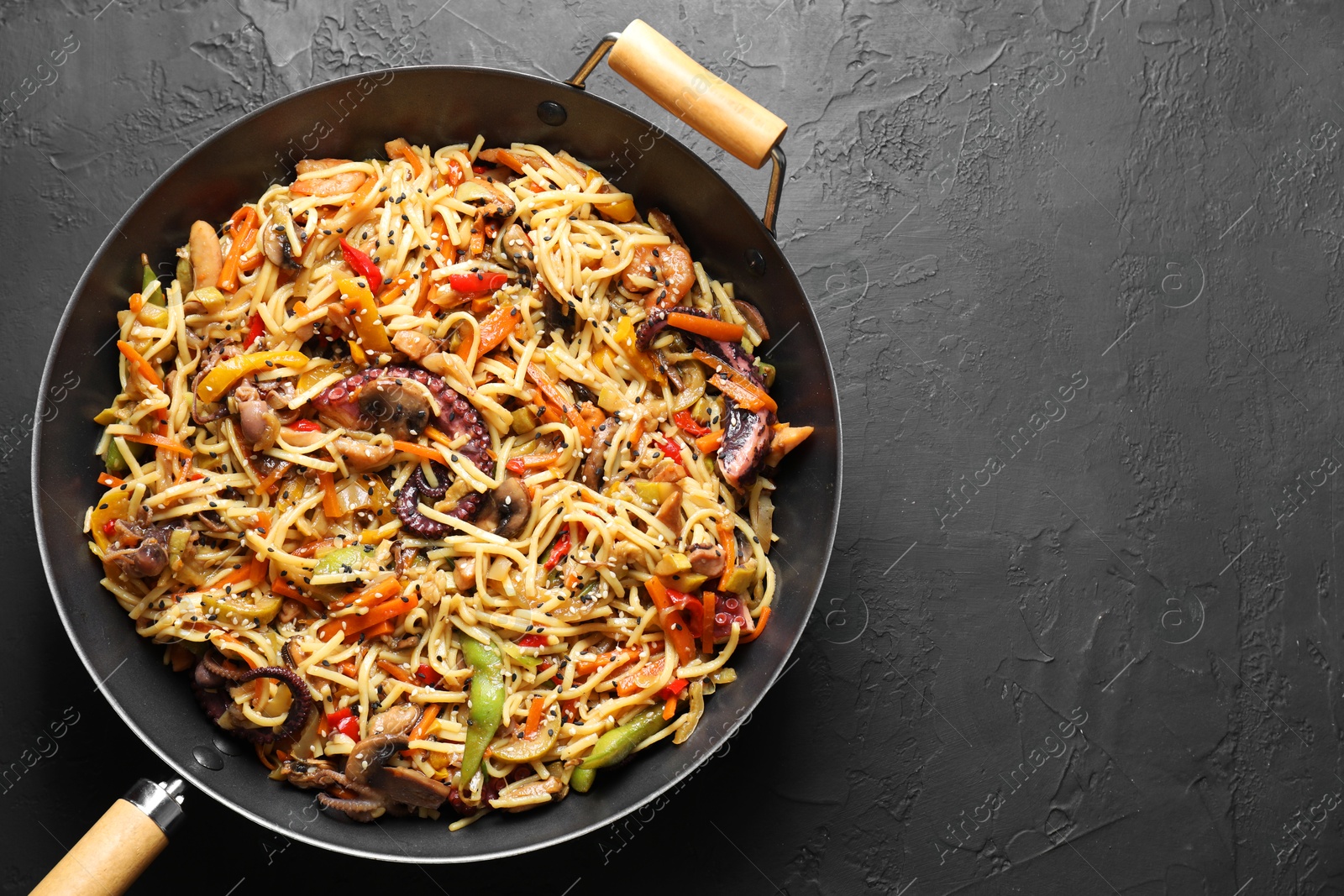 Photo of Stir-fry noodles with sea food and vegetables in wok on dark textured table, top view. Space for text