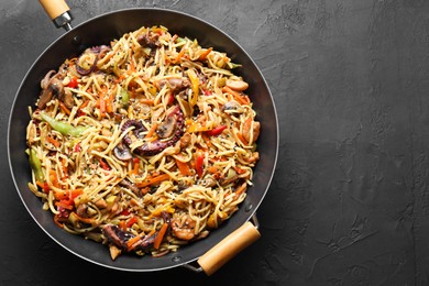 Stir-fry noodles with sea food and vegetables in wok on dark textured table, top view. Space for text