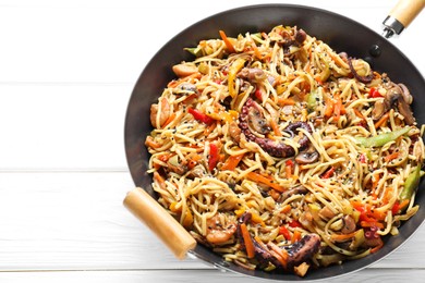 Stir-fry noodles with sea food and vegetables in wok on white wooden table, closeup. Space for text