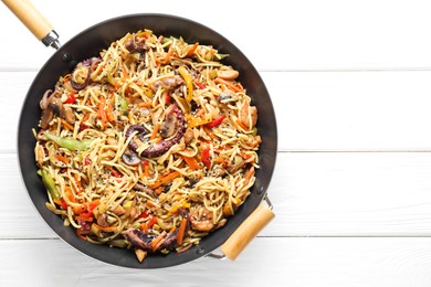 Stir-fry noodles with sea food and vegetables in wok on white wooden table, top view. Space for text